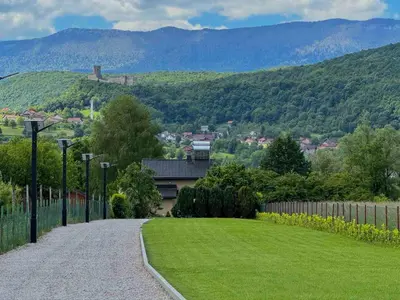 a driveway with a green lawn and mountains in the background at Sunrise Guest House in Bihać