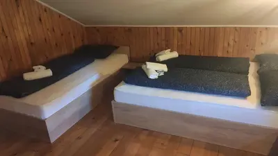 two beds in a room with wooden walls and wood floors at Sunrise Guest House in Bihać