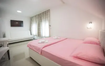 a white bedroom with a pink bed and a couch at Pansion Kipovi in Tuzla