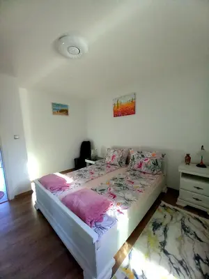 a bedroom with a white bed with pink sheets and a rug at Apartman Leon in Bihać
