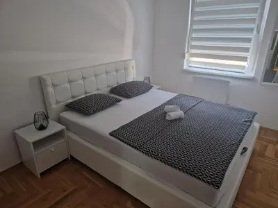 a white bed with a teddy bear sitting on it at Apartman 