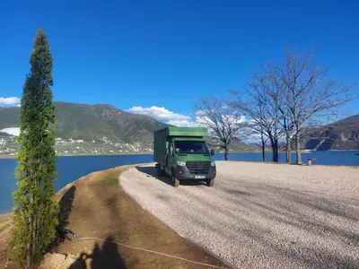 a green truck parked on a gravel road next to a lake at Auto Camping Grubeša in Dronjići