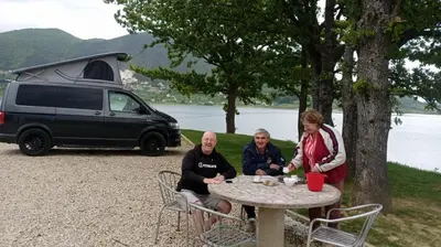 three people sitting at a table in front of a van at Auto Camping Grubeša in Dronjići