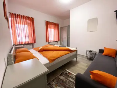 a bedroom with a bed with orange sheets and a couch at Soba za goste Kraljica 3 in Kupres