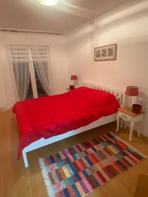 a bedroom with a red bed with a colorful rug at Moon Apartment Bihac in Bihać