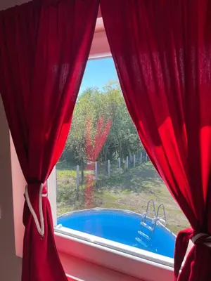 a window with red curtains and a view of a pool at Vikendica Villa Ramona Banja Luka in Banja Luka