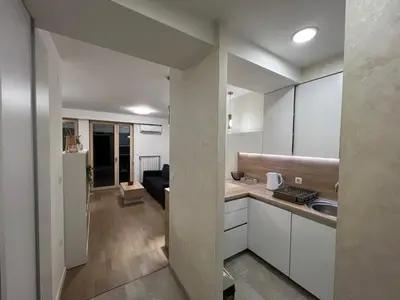 a kitchen with white cabinets and a living room at Apartman Sara in Zenica