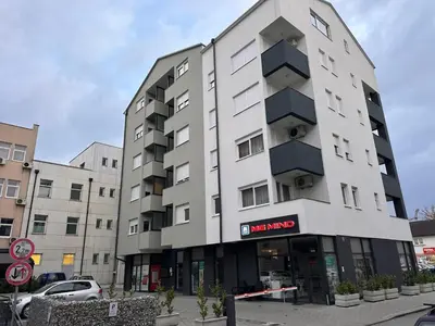a tall white building with a sign in front of it at Lux Apartment III Prijedor in Prijedor