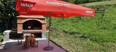 a outdoor pizza oven with a red umbrella and chairs at Eko kuca Jandro in Šipovo
