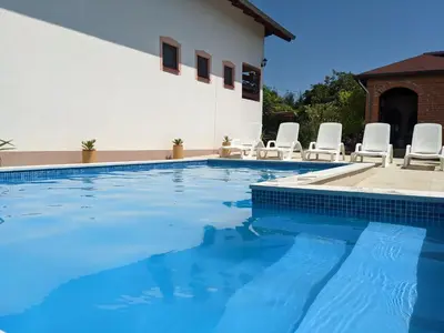 a swimming pool with chairs and a house at Wisteria Lodge in Derventa
