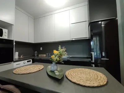 a kitchen with white cabinets and a table with a vase of flowers at Apartman Hajduković in Banja Luka