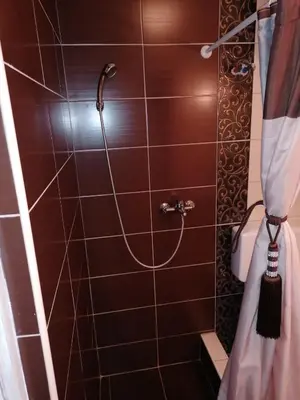 a shower in a bathroom with a brown tile wall at Apartmani Milica in Banja Luka