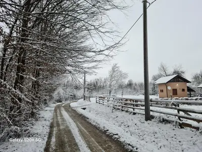 a snow covered road with a fence and a house at Vikendica 
