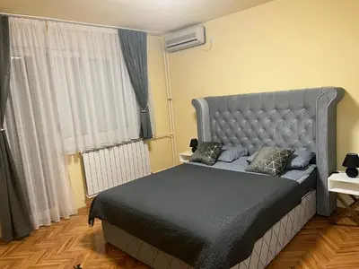 a bedroom with a bed with a gray headboard and a window at Apartman 2E in Tuzla