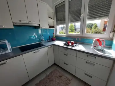 a kitchen with white cabinets and blue walls and windows at Apartman OMANOVIĆ in Bihać
