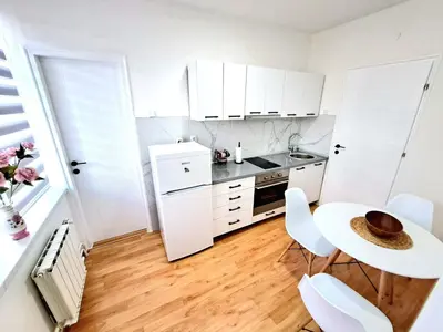a kitchen with white cabinets and a table and chairs at Apartman Skver Tuzla in Tuzla