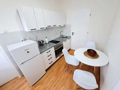 a white kitchen with a table and white chairs at Apartman Skver Tuzla in Tuzla