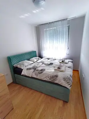 a bedroom with a bed with a green headboard and a window at Apartman D&D in Banja Luka