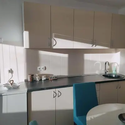 a kitchen with white cabinets and a blue chair at White home apartment in Banja Luka