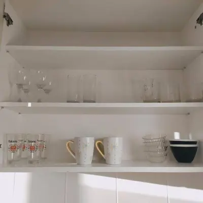 a white shelf with cups and glasses on it at White home apartment in Banja Luka