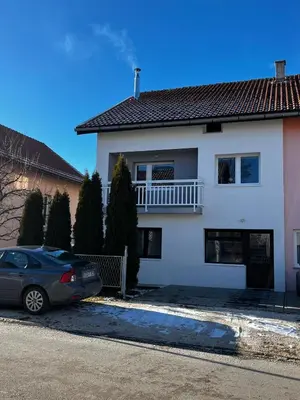 a white house with a car parked in the driveway at Apartman Lara in Kupres