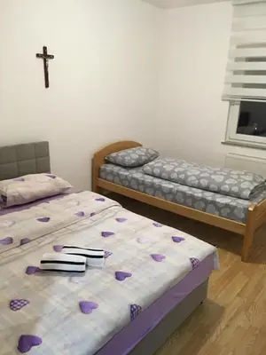 two beds in a room with a cross on the wall at Apartman Lara in Kupres