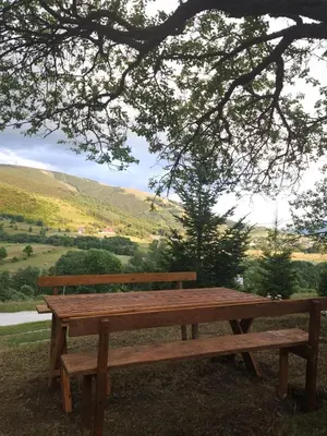 a wooden bench sitting in the grass under a tree at Planinska kuća Ruža in Kupres