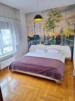 a bedroom with a large bed with a painting on the wall at San apartment in Banja Luka