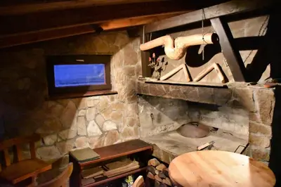 a room with a stone fireplace with a television and a wooden table at Villa Šola in Kupres