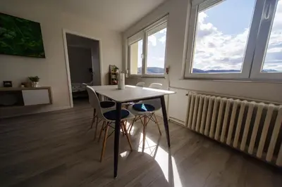 a dining room with a table and chairs and two windows at 5 min Apartment in Banja Luka