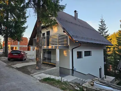 a white house with a black roof and a car at Apartman Flora Vlasic in Vlasic