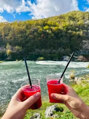 two hands holding two glasses of red liquid with sticks at Aqua Vita Concept in Bihać