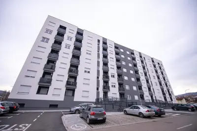 a large white building with cars parked in a parking lot at Apartman Mihalena in Banja Luka