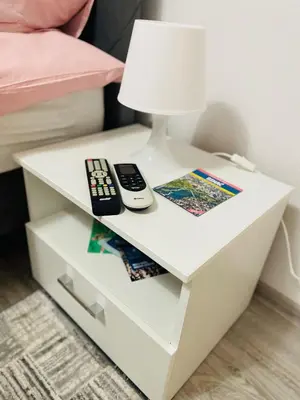 a white nightstand with two remote controls and a lamp at Apartment Zara Bihac in Bihać