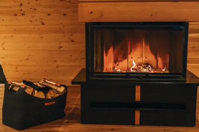 a fireplace in a room with a basket of logs at The Cozy Chalet in Bosanski Petrovac