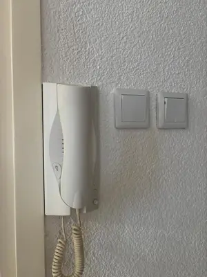 a white hair dryer on a wall next to two switches at APARTMAN ADI in Jajce