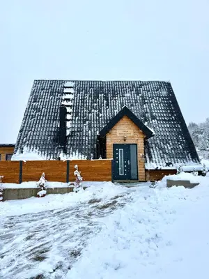 a wooden building with a black roof in the snow at Kuća za odmor Villa Kovačević in Bihać