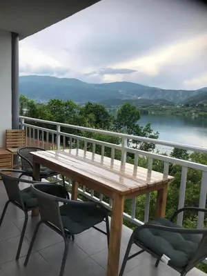 a wooden table and chairs on a balcony with a view of a lake at Apartman Manov - Ramsko jezero in Prozor