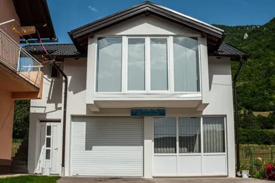a white house with a large window and a garage at Guest House Šobić in Šipovo