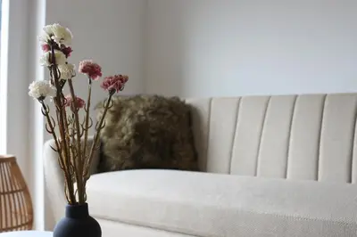 a vase with flowers on a table next to a couch at West Wing - Apartmani Živinice in Živinice