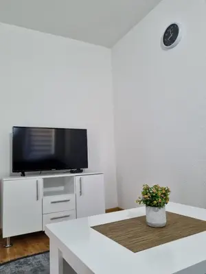 a white living room with a tv and a table at Apartman CENTAR 1 in Jajce
