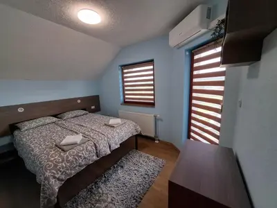 a bedroom with a bed and a table and two windows at Djuric Vacation House in Laktaši