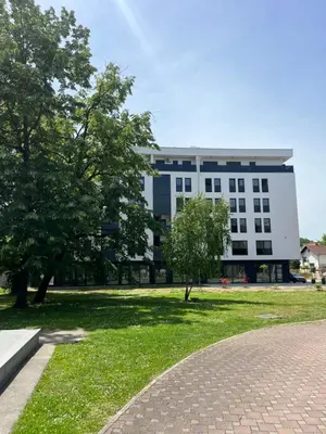 a large white building with trees in front of it at Green Lux Apartman Prijedor in Prijedor