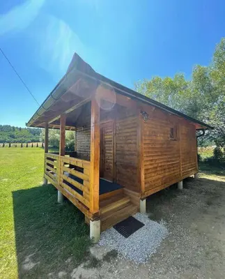 a wooden cabin with a roof on a grass field at Etno zona Oaza mira in Donji Vakuf