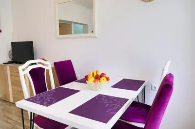 a dining room table with purple chairs and a bowl of fruit at Apartman SUMI in Bihać