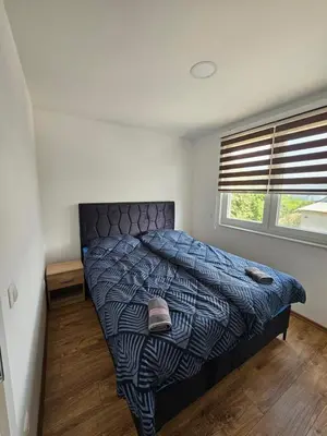 a bedroom with a bed with a blue comforter and a window at Apartmani gradina Tuzla in Tuzla