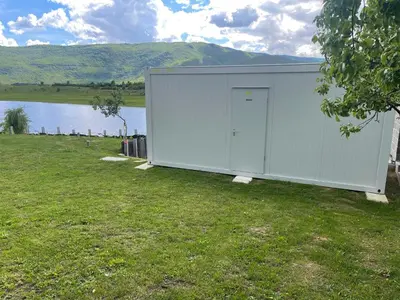 a large white building in the grass next to a body of water at Camp Tommy in Jaklići