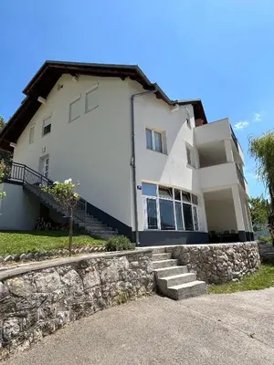 a large white house with a stone wall at Apartmani Venecia in Prozor