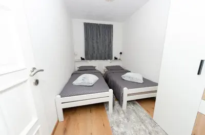 two beds in a room with white walls and wooden floors at Apartment Center Korzo in Bihać