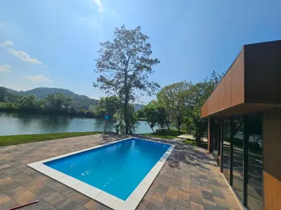 a swimming pool next to a house with a lake at Villa Vigo in Bosanska Krupa